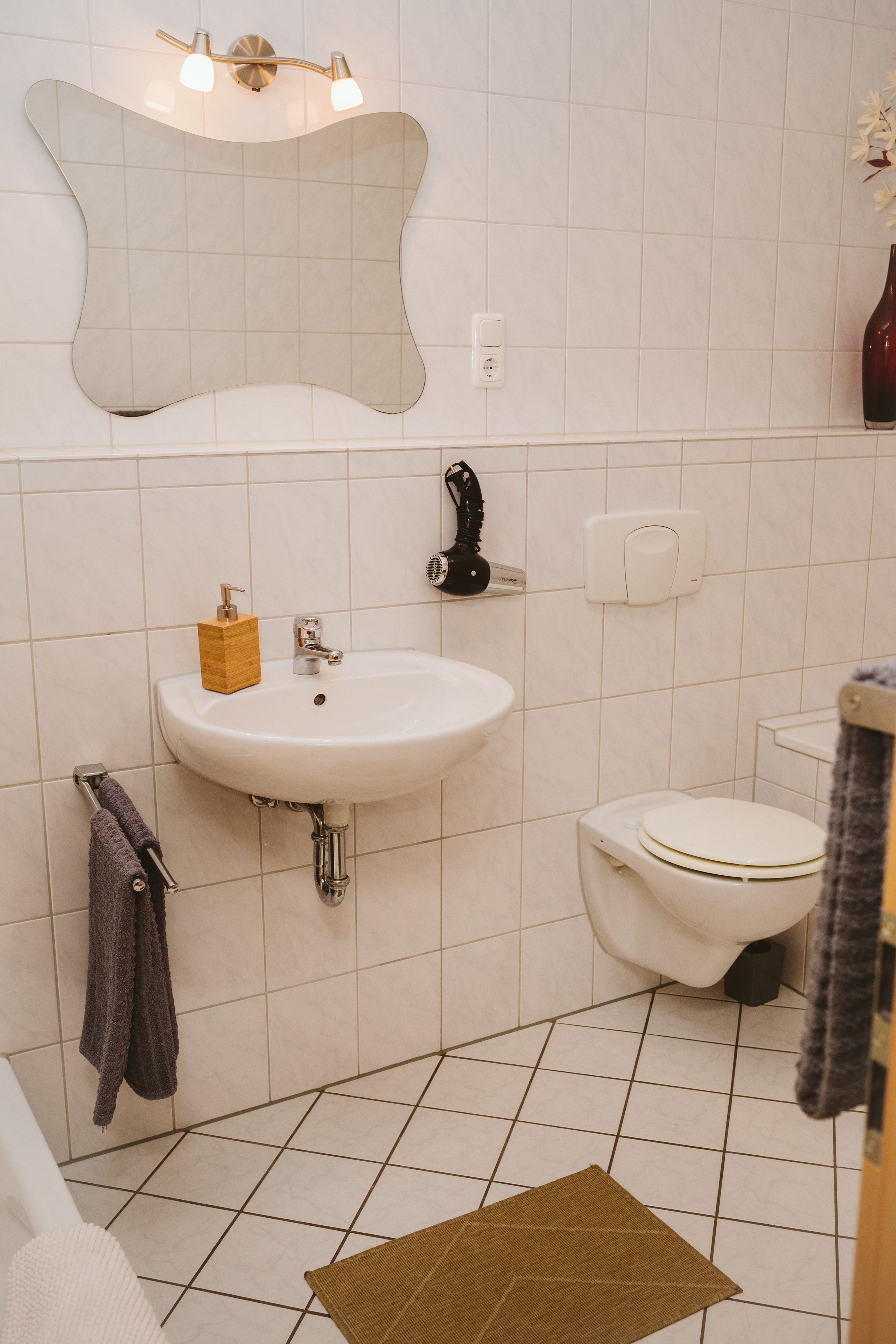 Ein Badezimmer mit einem weißen Waschbecken, einer Toilette, einem Spiegel und einem Handtuchhalter.