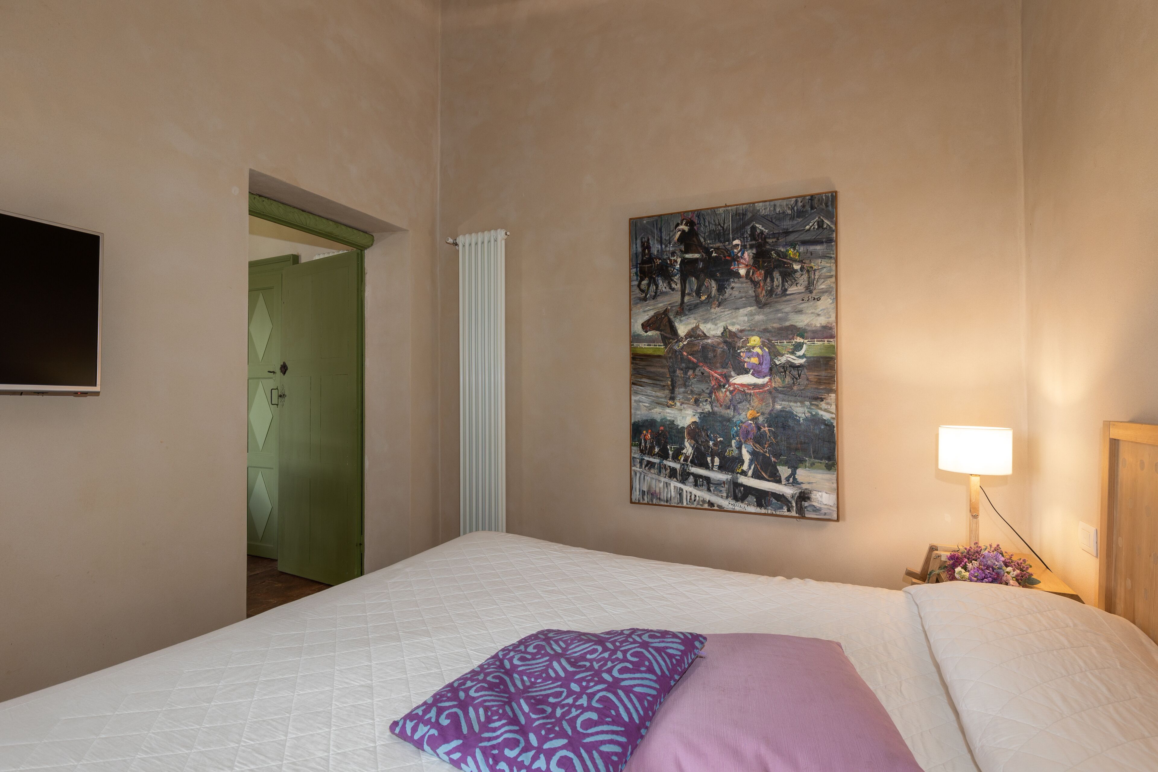 A bedroom with a bed, a painting on the wall, a lamp, and a door.