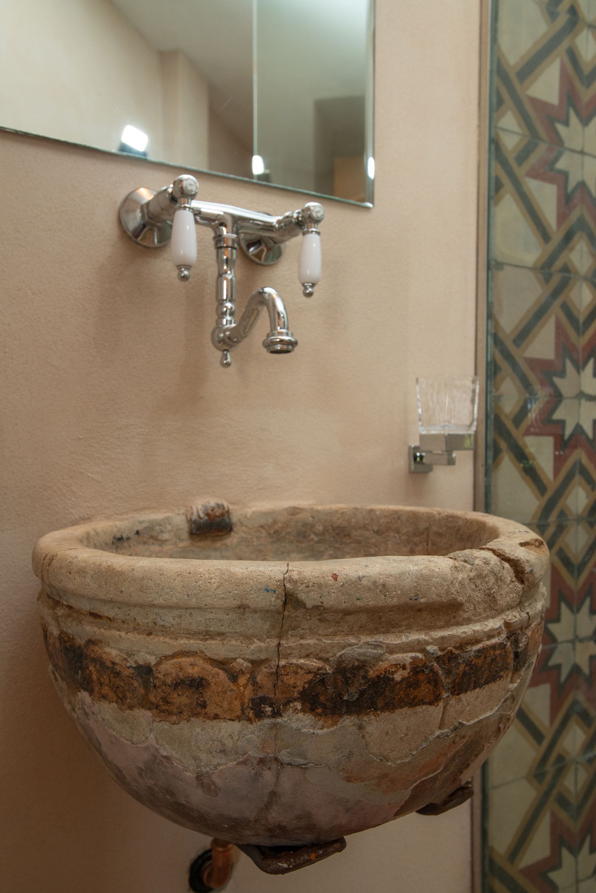 A bathroom with a large, rustic stone sink, a modern faucet, and a mirror above it.