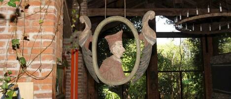 Una habitación rústica con una escultura colgante, paredes de ladrillo y vistas al verdor exterior.