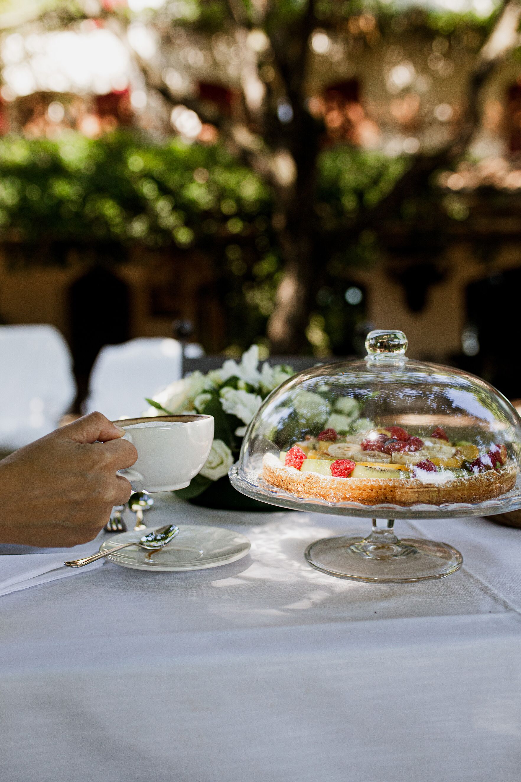 A dessert on a glass stand with a spoon and a cup beside it.
