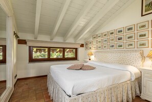 A bedroom with a large bed, a window with a view, and a wall decorated with framed pictures. - La Cucchetta (Dormelletto)