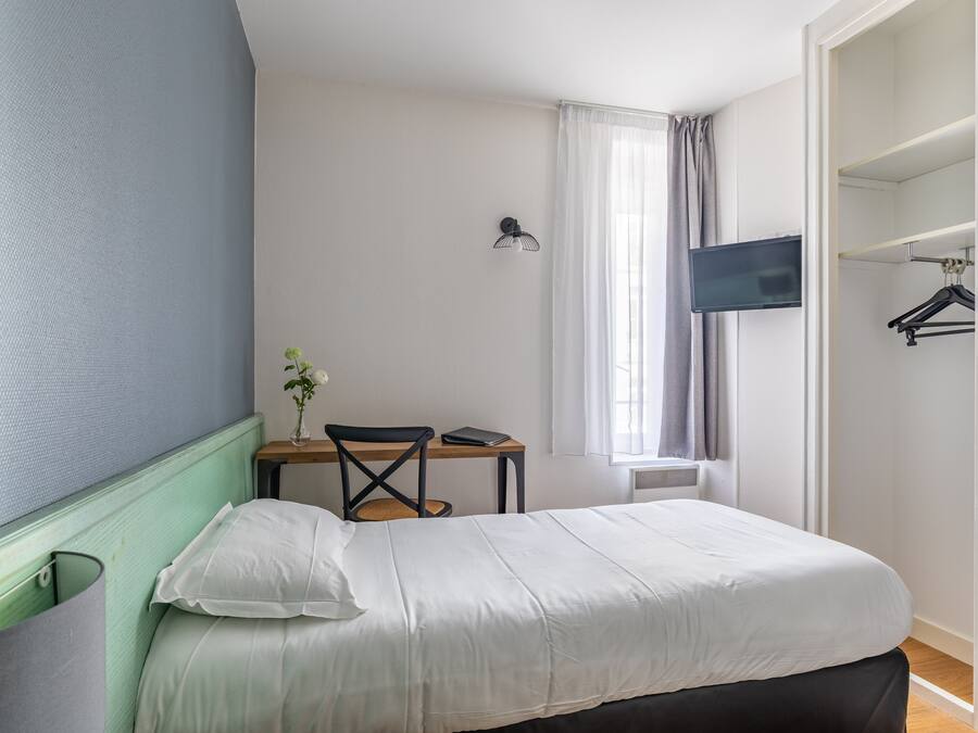 Une chambre à coucher avec un lit, un bureau avec une chaise, une télévision et une armoire.