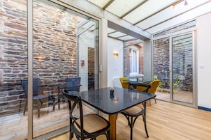 Un intérieur moderne avec une table et des chaises en verre, des murs en pierre et une vue dégagée grâce à de grandes portes vitrées.