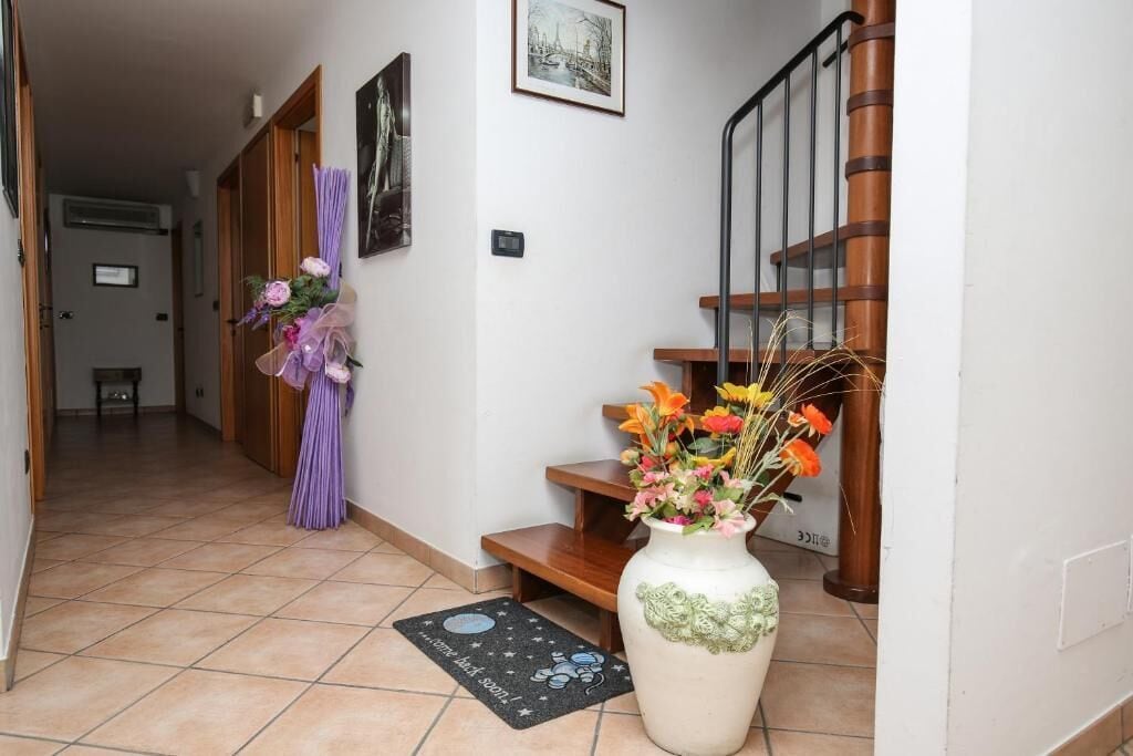 A hallway with a wooden staircase, a vase with flowers, and a doormat.