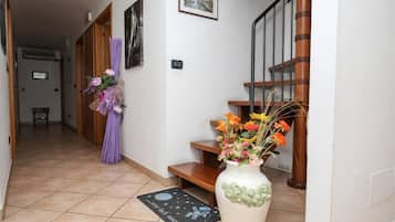 A hallway with a wooden staircase, a vase with flowers, and a doormat.