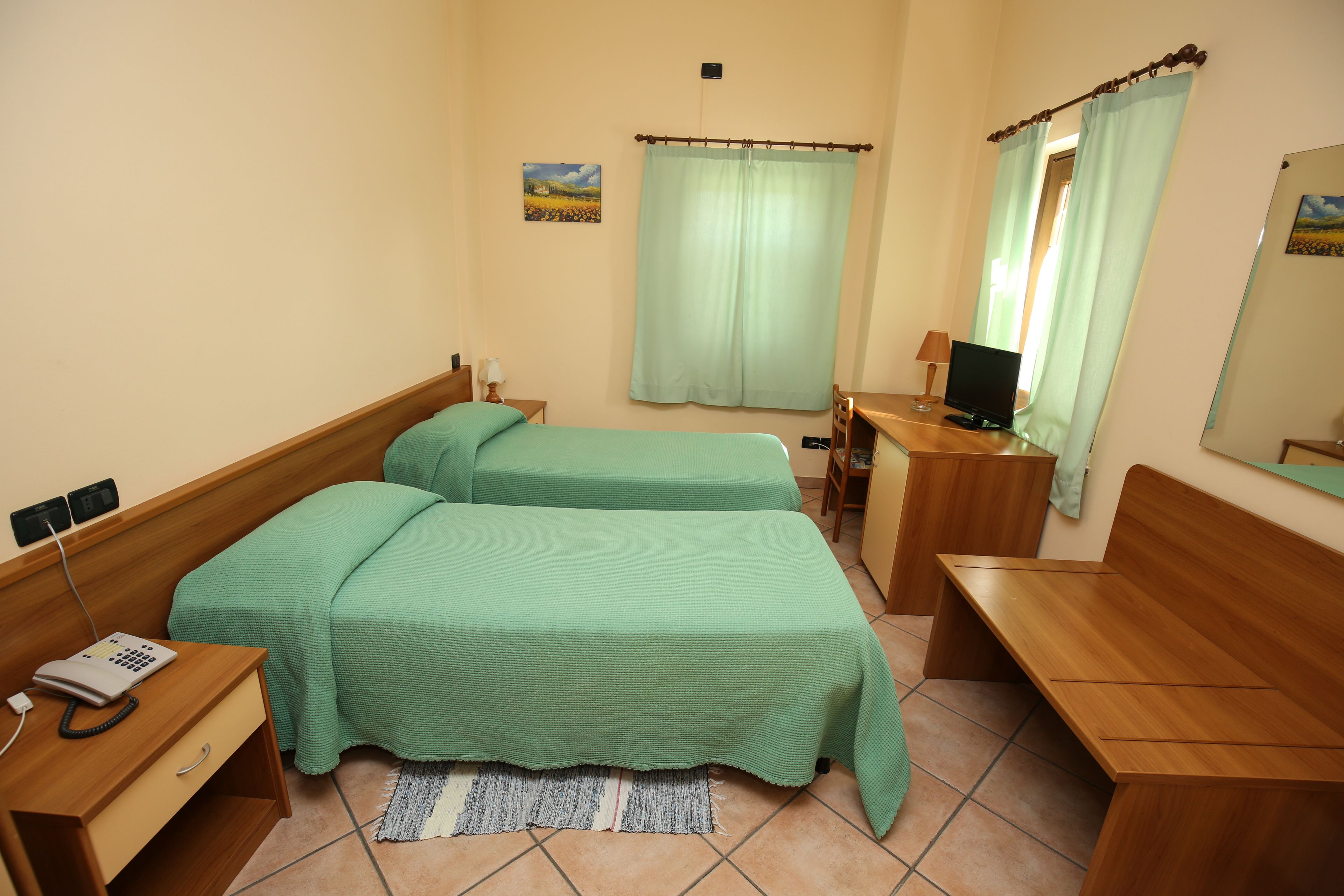 Habitació d'hotel amb dos llits, un escriptori, una cadira, un telèfon i un mirall.