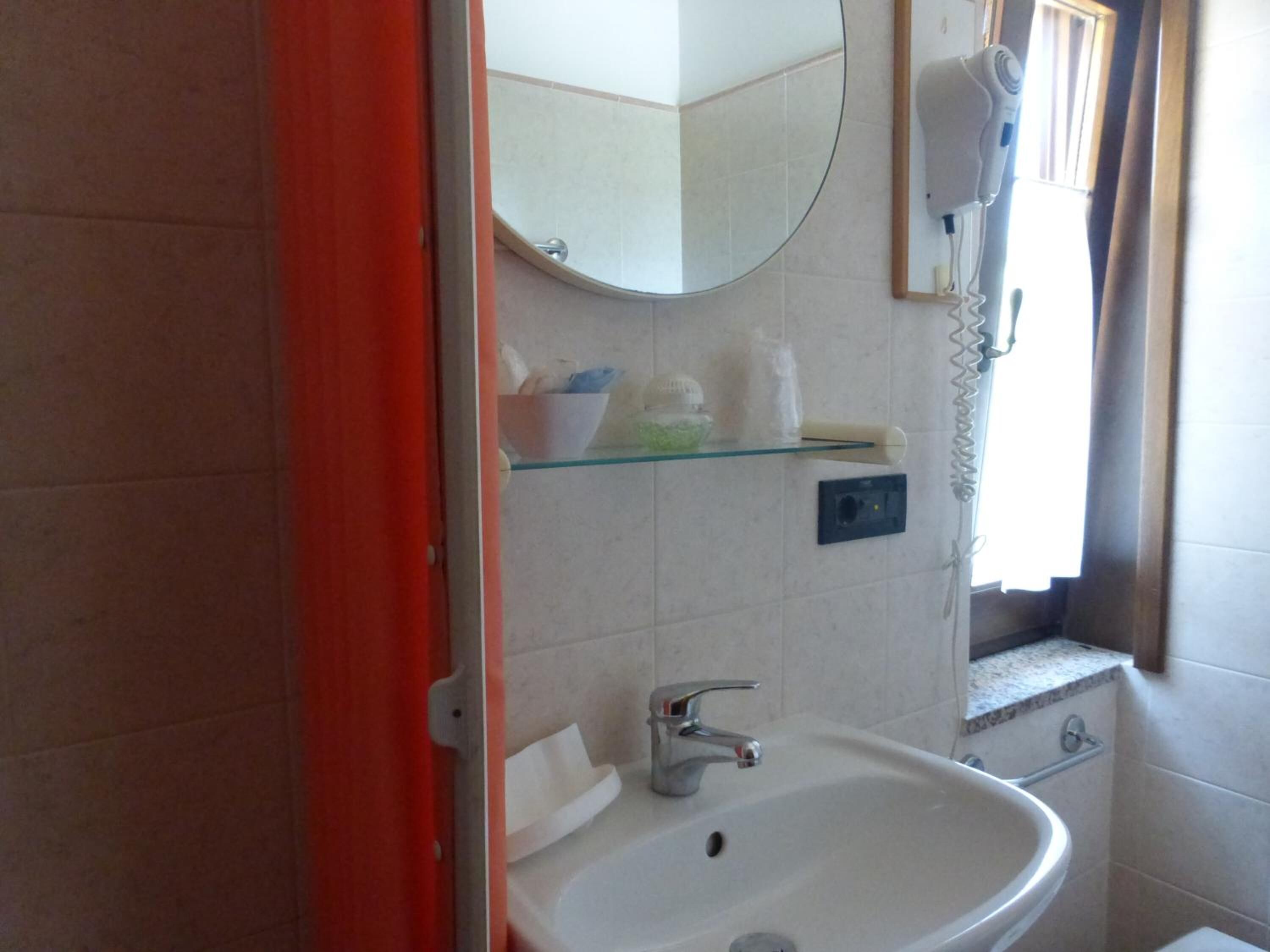 Un baño con un lavamanos blanco, un espejo y un secador de pelo en la pared.