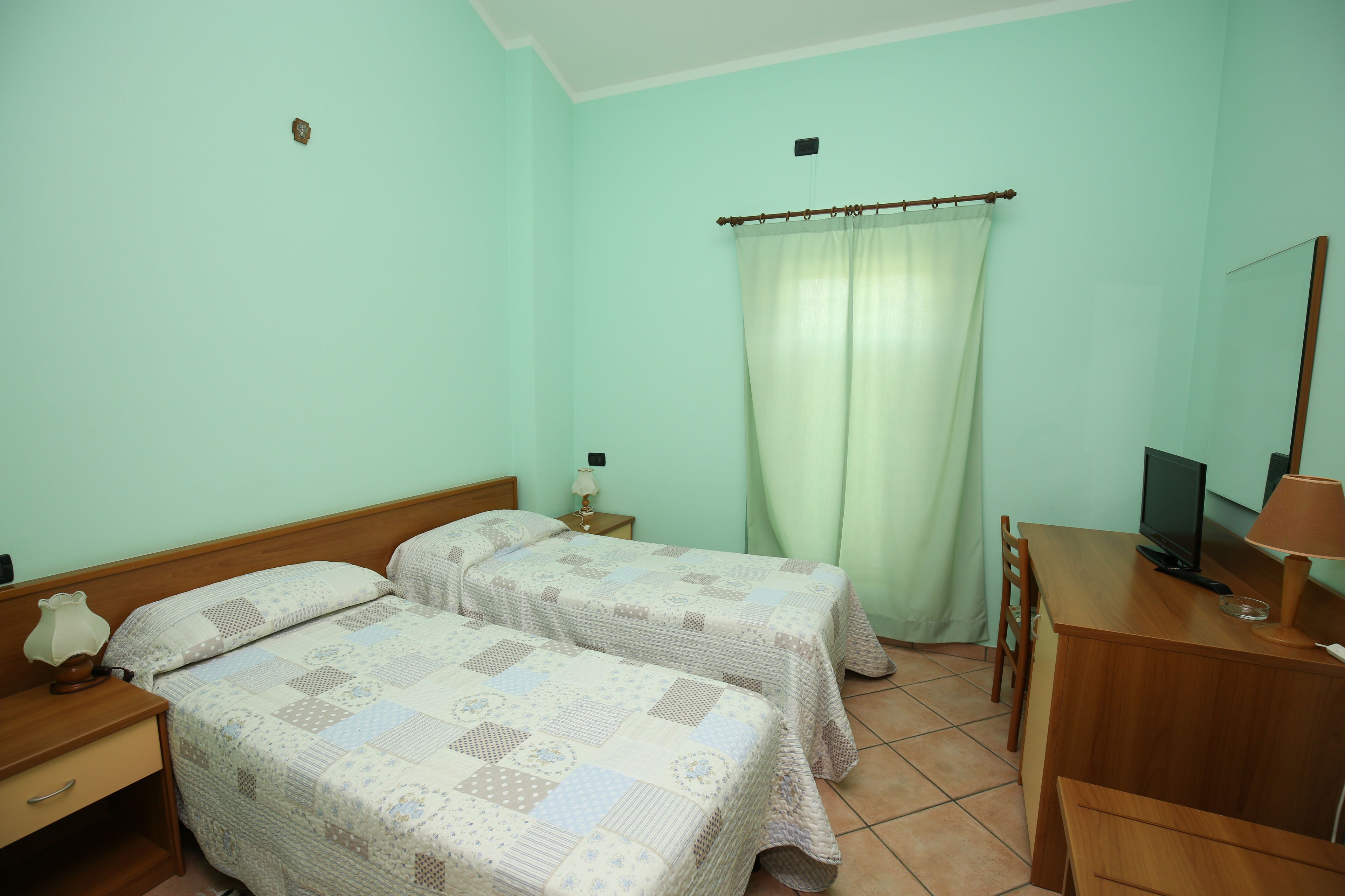A room with two beds, a desk, a chair, a television, and a curtain.