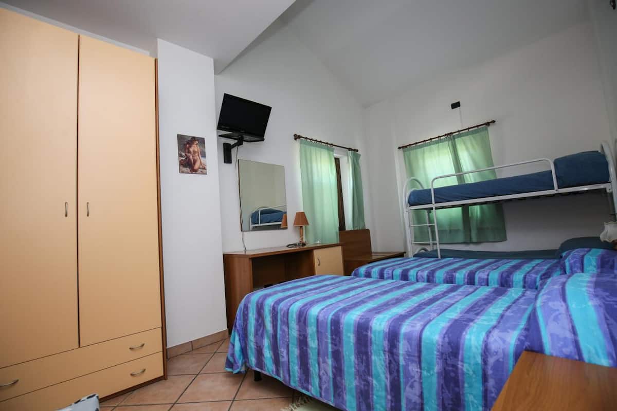A dormitory room with bunk beds, a desk, a chair, a television, and a wardrobe.