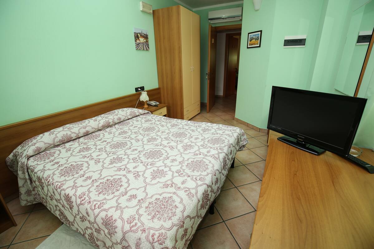 A bedroom with a bed, a TV, a wardrobe, and a desk.