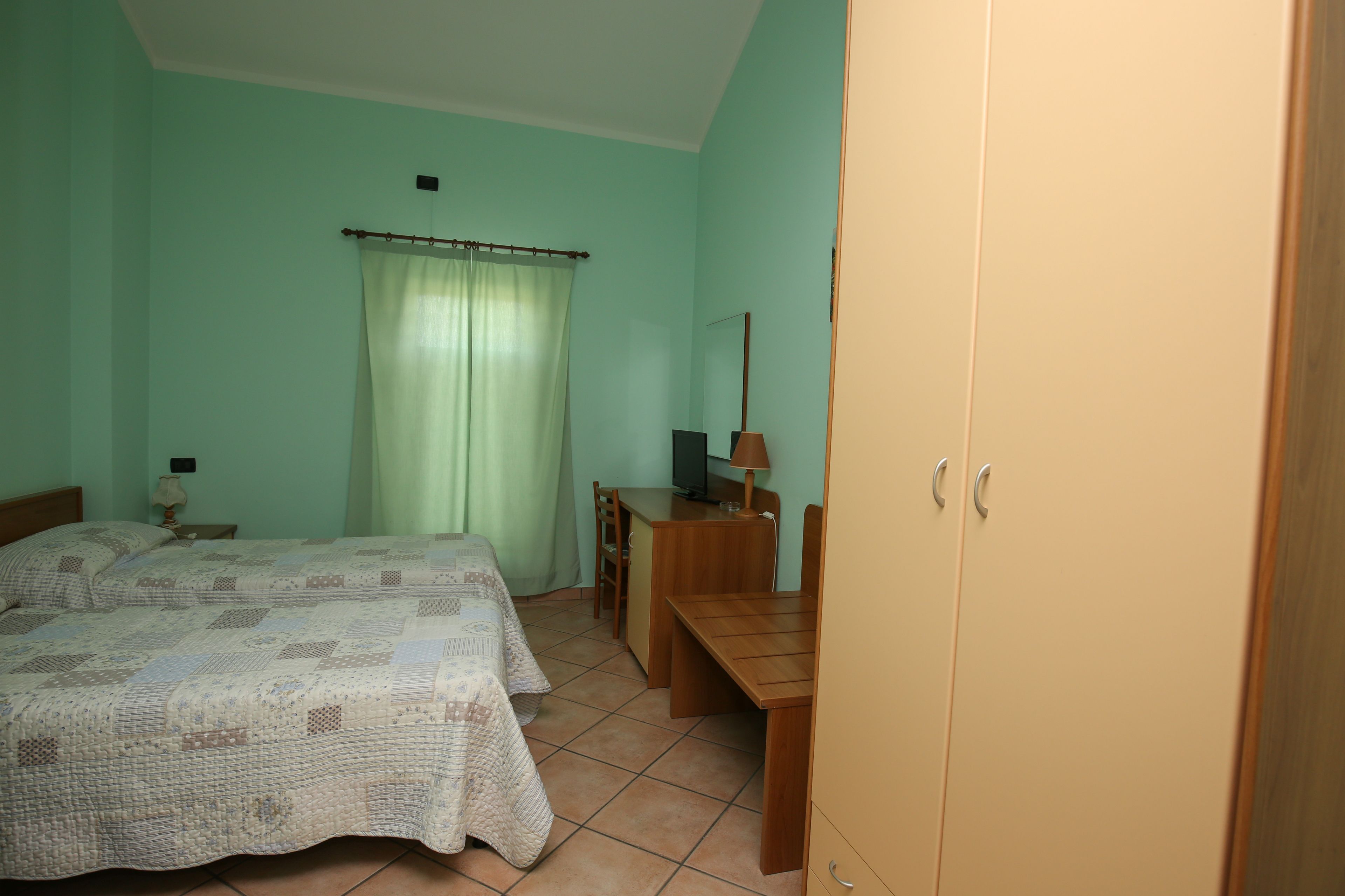 A room with two beds, a desk, a chair, a lamp, and a wardrobe.