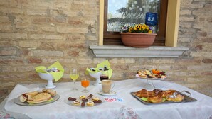 A breakfast table with pastries, sandwiches, and drinks, set against a stone wall. - Al Casolare (Corinaldo)