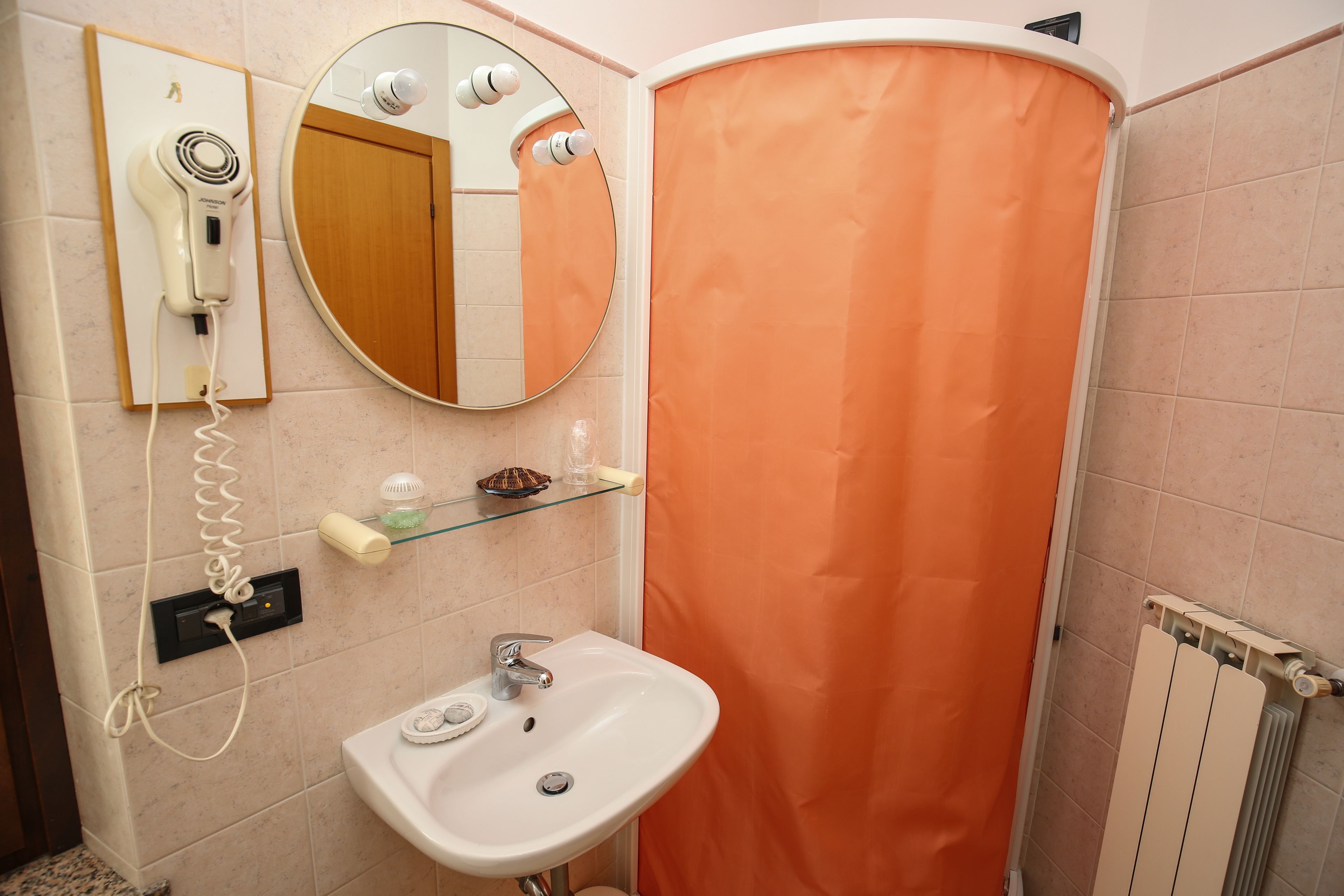 A bathroom with a white sink, a hairdryer mounted on the wall, a mirror, and an orange shower curtain.