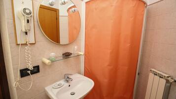 A bathroom with a white sink, a hairdryer mounted on the wall, a mirror, and an orange shower curtain.