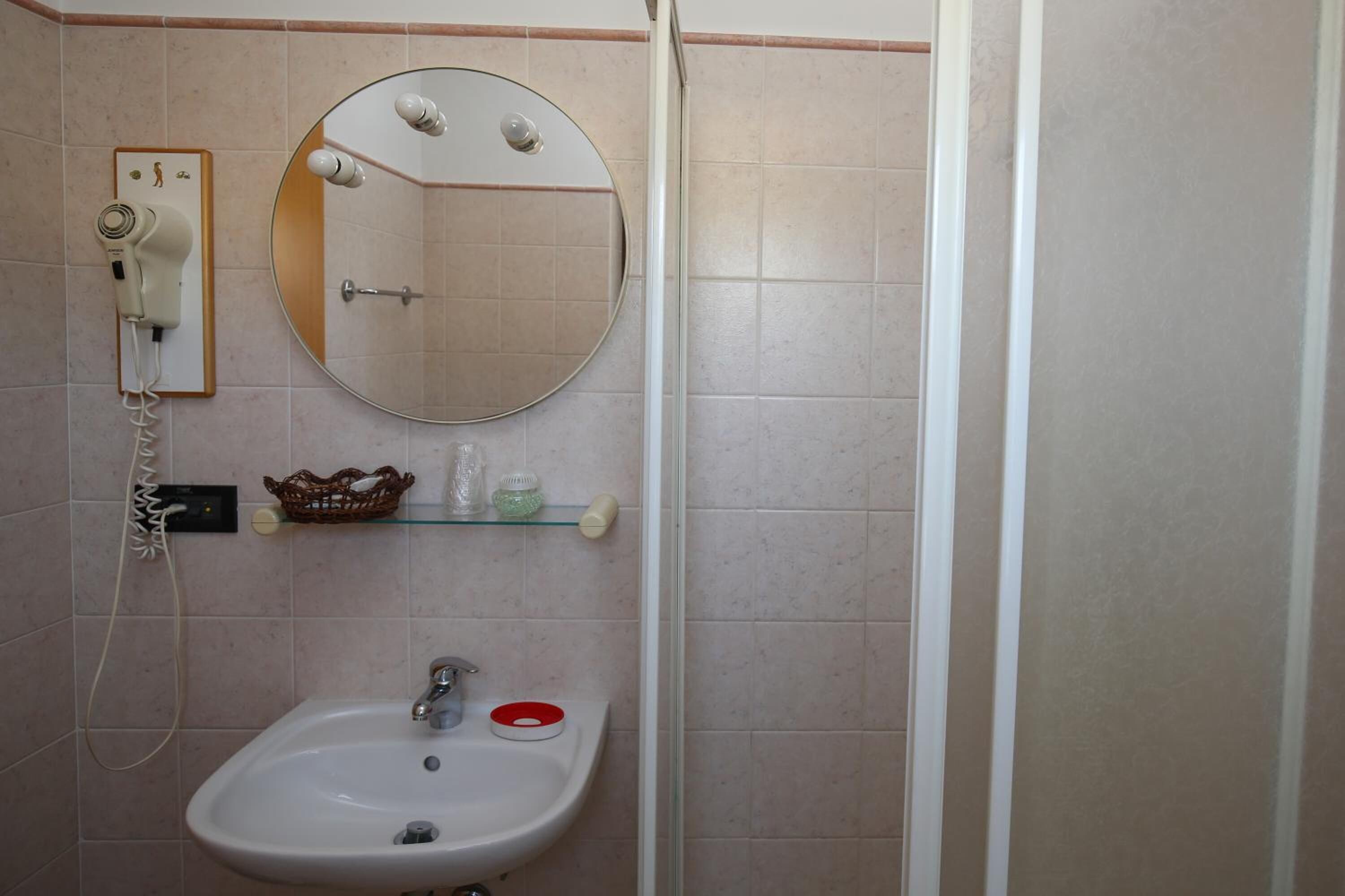 Un baño con lavamanos, espejo, secador de pelo y cabina de ducha.