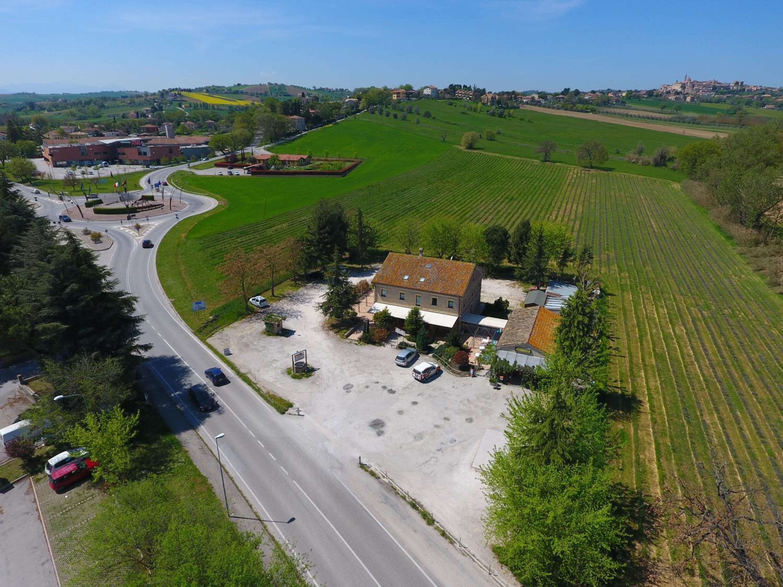 An aerial view of a rural area with a building surrounded by fields, a road, and a small parking area.