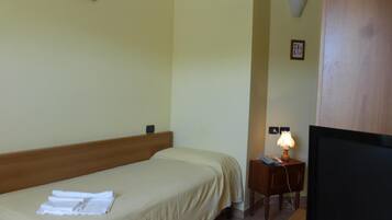 Habitación de hotel con cama, mesita de noche con lámpara, televisor y un pequeño marco con fotografía en la pared.