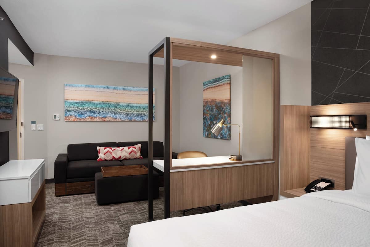 Una habitación de hotel moderna con una cama, un escritorio, un sofá y un espejo grande.