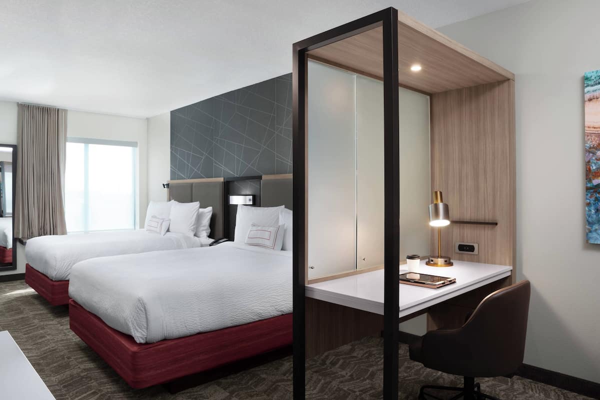 Una habitación de hotel con dos camas, un escritorio y un espejo grande.