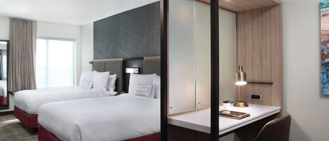 A hotel room with two beds, a desk, and a large mirror.