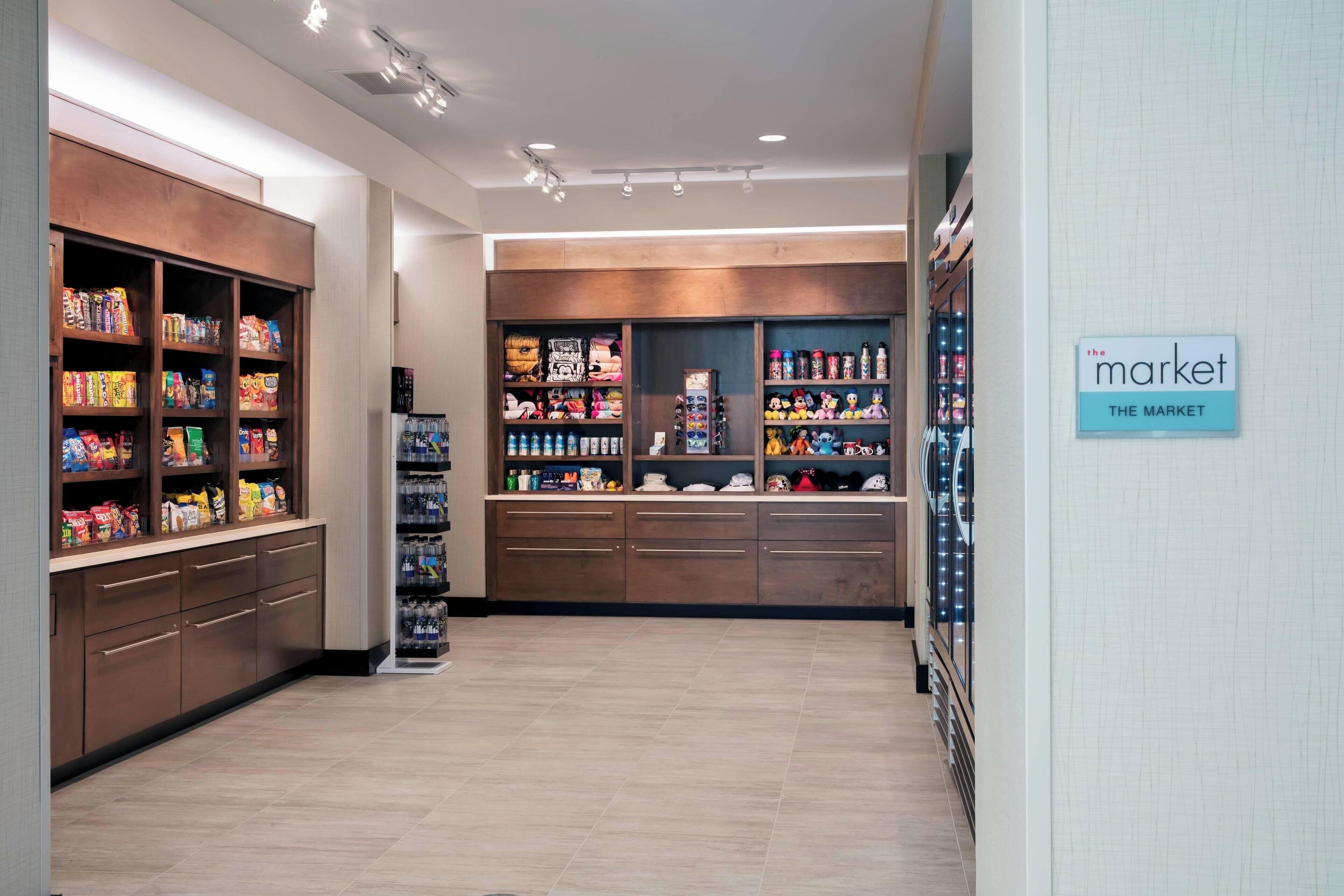 A well-lit store with shelves stocked with snacks and beverages, a refrigerated section, and a sign indicating 'The Market'.