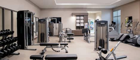 Un gimnasio con diversos equipos de ejercicio, incluyendo pesas, una banca y máquinas de cardio.