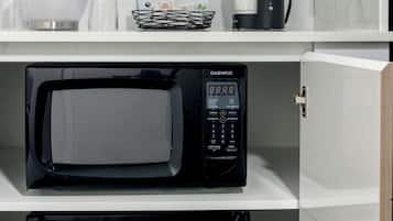Una cocina compacta con un refrigerador de acero inoxidable, un microondas negro y una cafetera sobre la encimera.