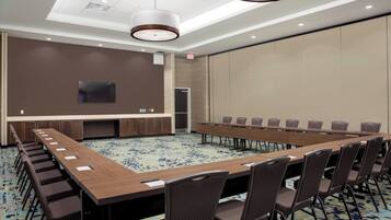 A conference room with a long table, chairs, a flat-screen TV, and a carpeted floor.