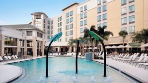 A hotel pool area with lounge chairs, a water fountain, and a building with multiple floors and windows. - SpringHill Suites by Marriott Orlando Theme Parks/Lake Buena Vista (Orlando)