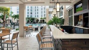 A bar area with a long counter, seating with wooden chairs, and a pool view. - SpringHill Suites by Marriott Orlando Theme Parks/Lake Buena Vista (Orlando)