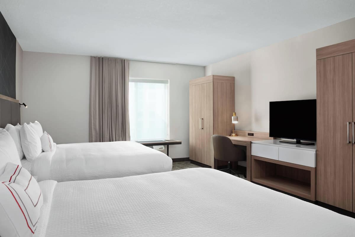Habitación de hotel con dos camas, un escritorio con televisor y un armario.