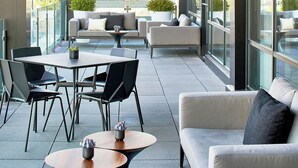 An outdoor seating area with tables and chairs, a sofa, and a potted plant. - AC Hotel by Marriott Cleveland Beachwood (Orange)