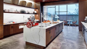 A modern kitchen with marble countertops, wooden cabinets, and a large island with a red wheel. - AC Hotel by Marriott Cleveland Beachwood (Orange)