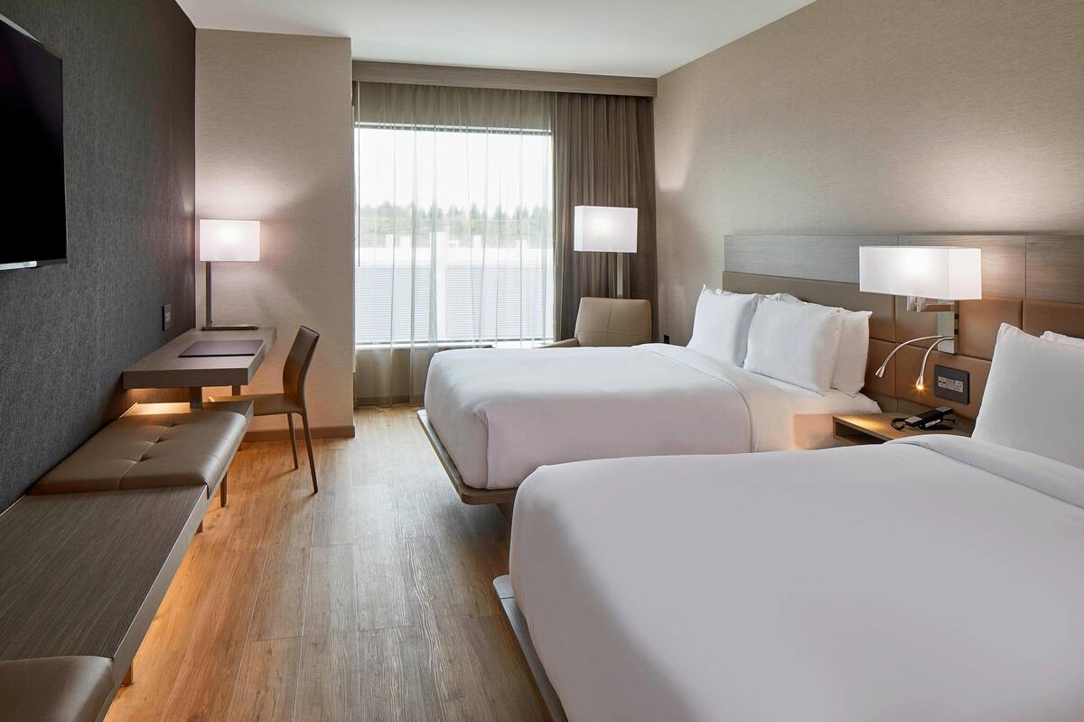 A hotel room with two beds, a desk, a chair, and a TV.