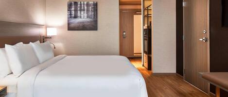 Ein modernes Hotelzimmer mit einem großen Bett, einem Nachttisch, einer Wandlampe und einem Gemälde.