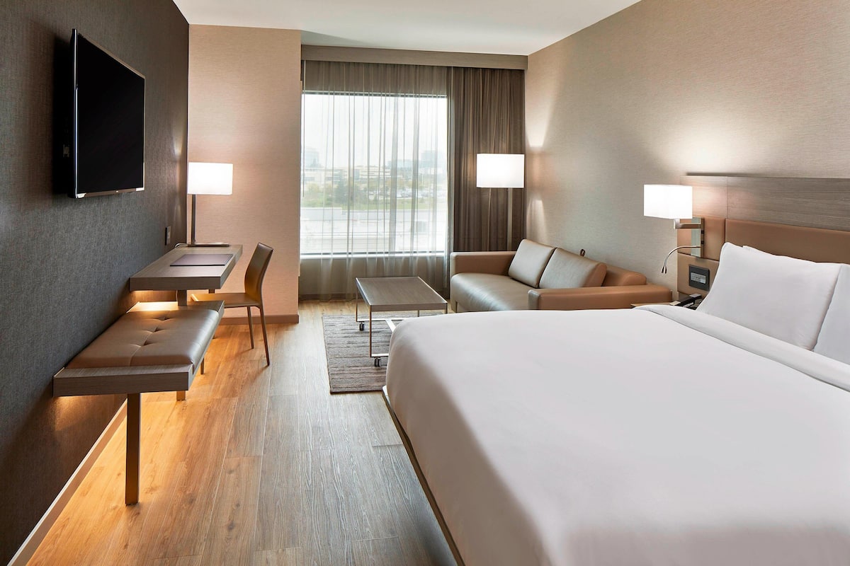 A hotel room with a large bed, a desk with a chair, a sofa, and two bedside lamps.