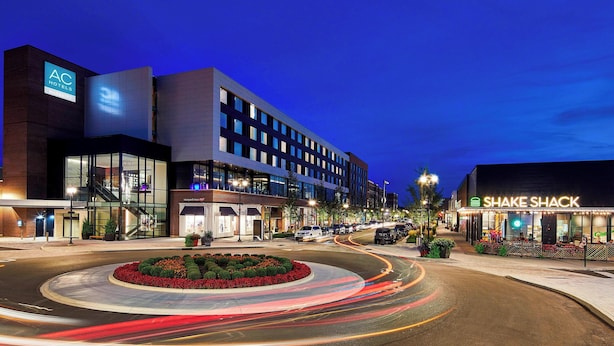 A modern hotel with a prominent AC logo, a Shake Shack, and a landscaped roundabout. - AC Hotel by Marriott Cleveland Beachwood (Orange)