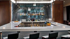 A bar area with a marble countertop, shelves with bottles, and bar stools. - AC Hotel by Marriott Cleveland Beachwood (Orange)