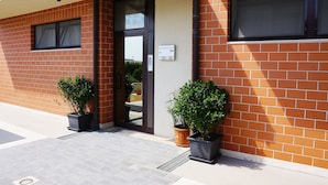 A modern building with a brick facade, a glass door entrance, and two potted plants on the ground. - B&B President's Home (Matera)