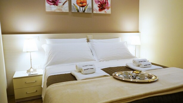 A neatly made hotel room with a large bed, two bedside lamps, a tray with breakfast items, and towels with the hotel's name. - B&B President's Home (Matera)
