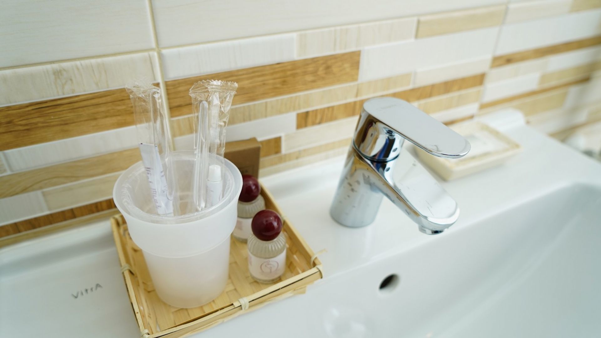 A bathroom sink with a chrome faucet, a white basin, and a wooden tray holding a toothbrush, toothpaste, and a small bottle.