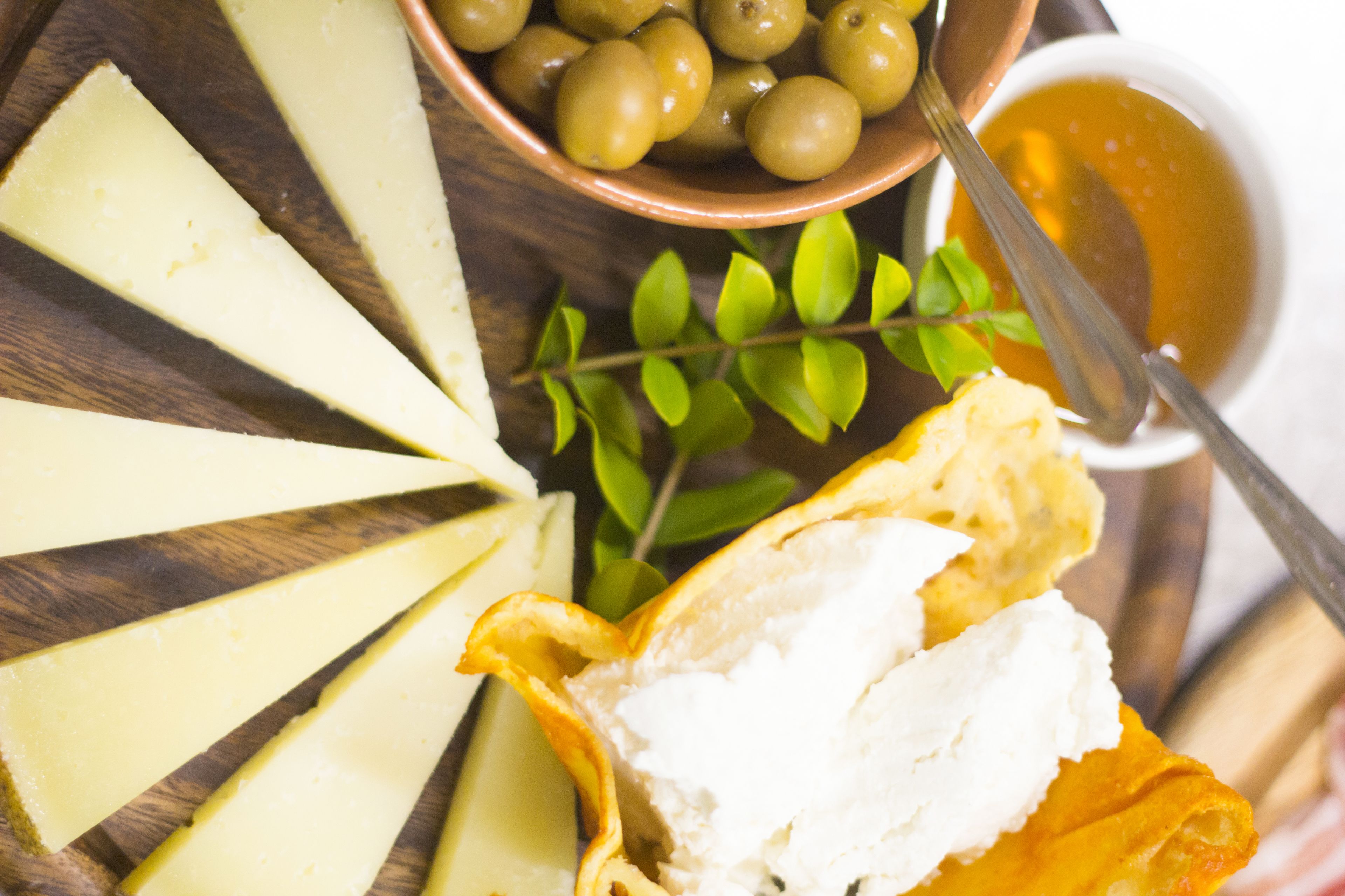 Une planche en bois garnie de tranches de fromage, d’olives et d’un bol de soupe.