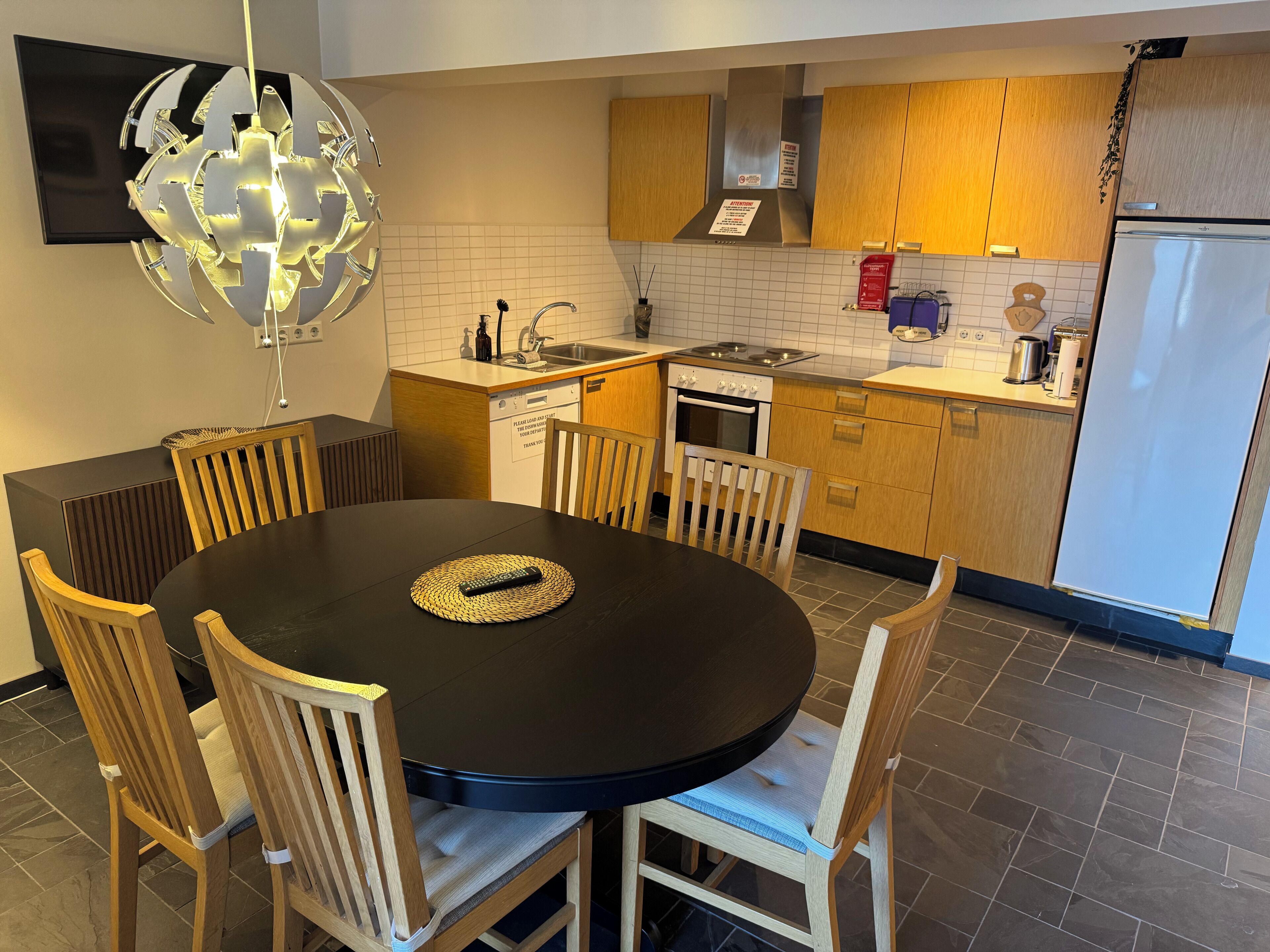 Een moderne keuken met een eettafel, stoelen, een televisie en een koelkast.