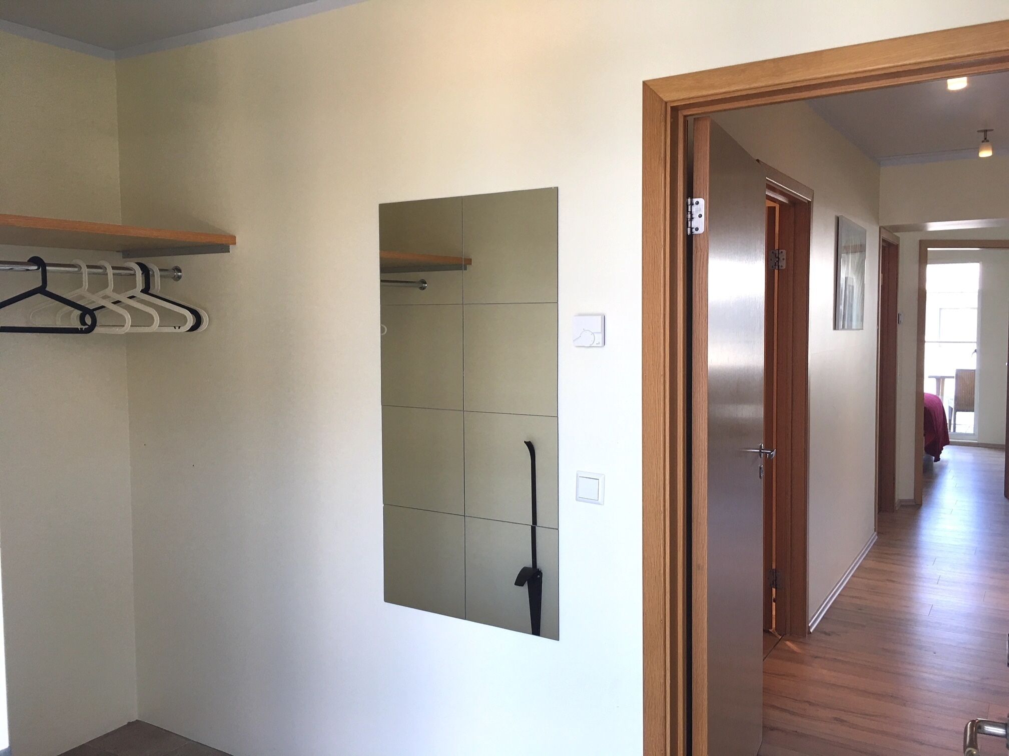 A hallway with a wooden door, a coat rack, and a mirror on the wall.