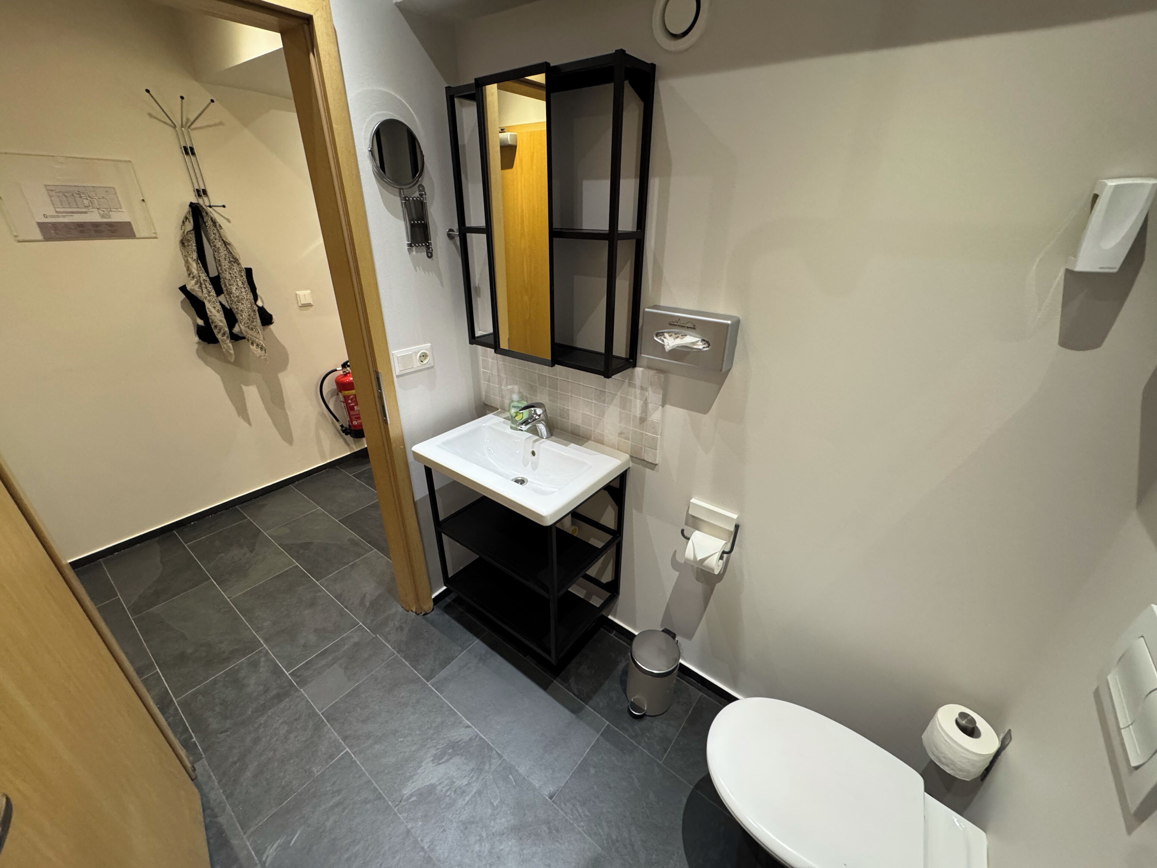 Ein Badezimmer mit Waschbecken, Spiegel, Toilette und Handtuchspender.
