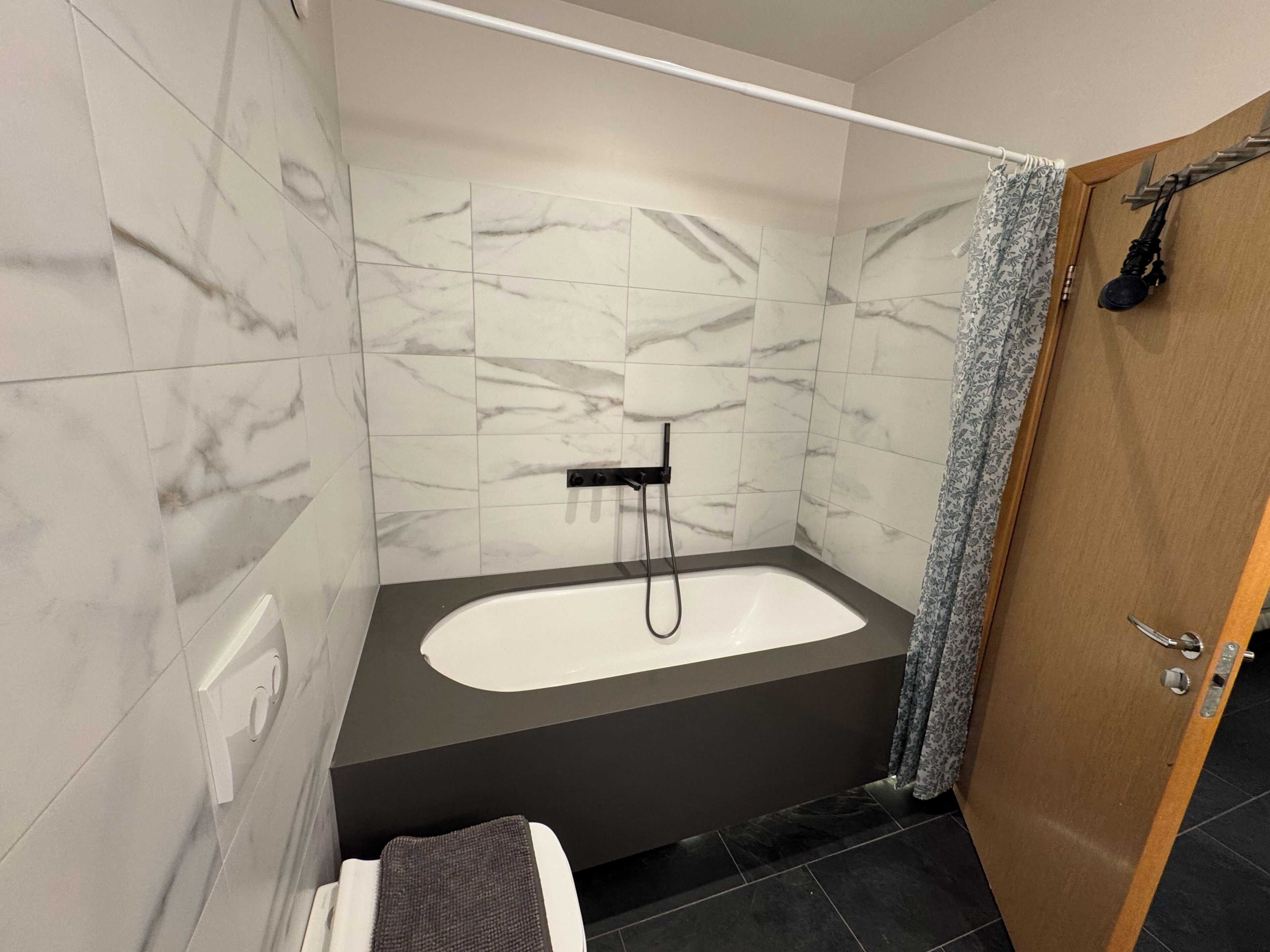A modern bathroom with a freestanding bathtub, a showerhead, and a wooden door.