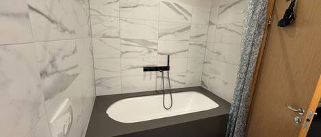A modern bathroom with a freestanding bathtub, a showerhead, and a wooden door.
