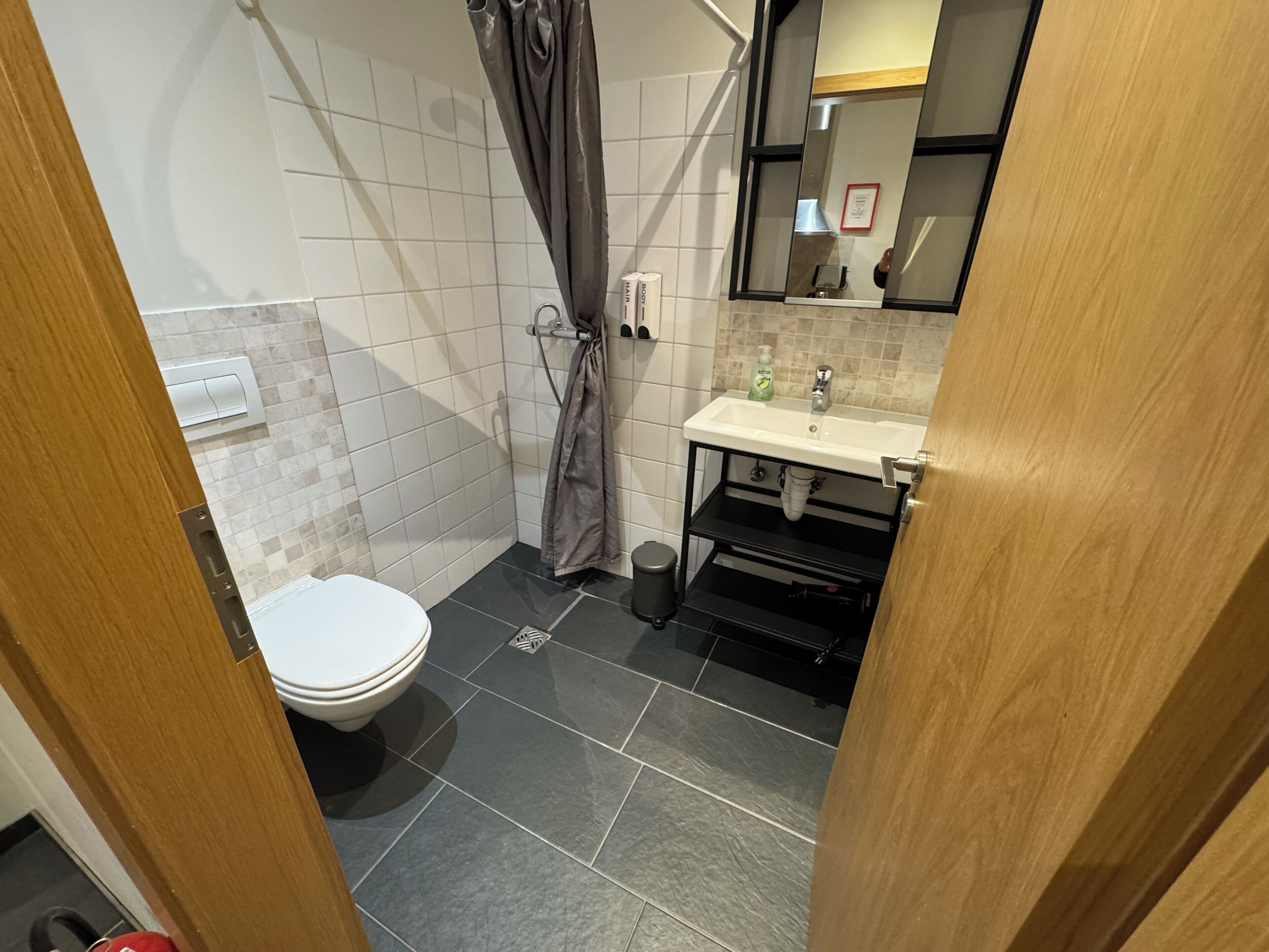 A bathroom with a toilet, a shower with a curtain, a sink with a mirror, and tiled walls.