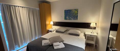 Una habitación de hotel con una cama grande, dos mesitas de noche con lámparas, un cuadro en la pared y una ventana con cortinas.